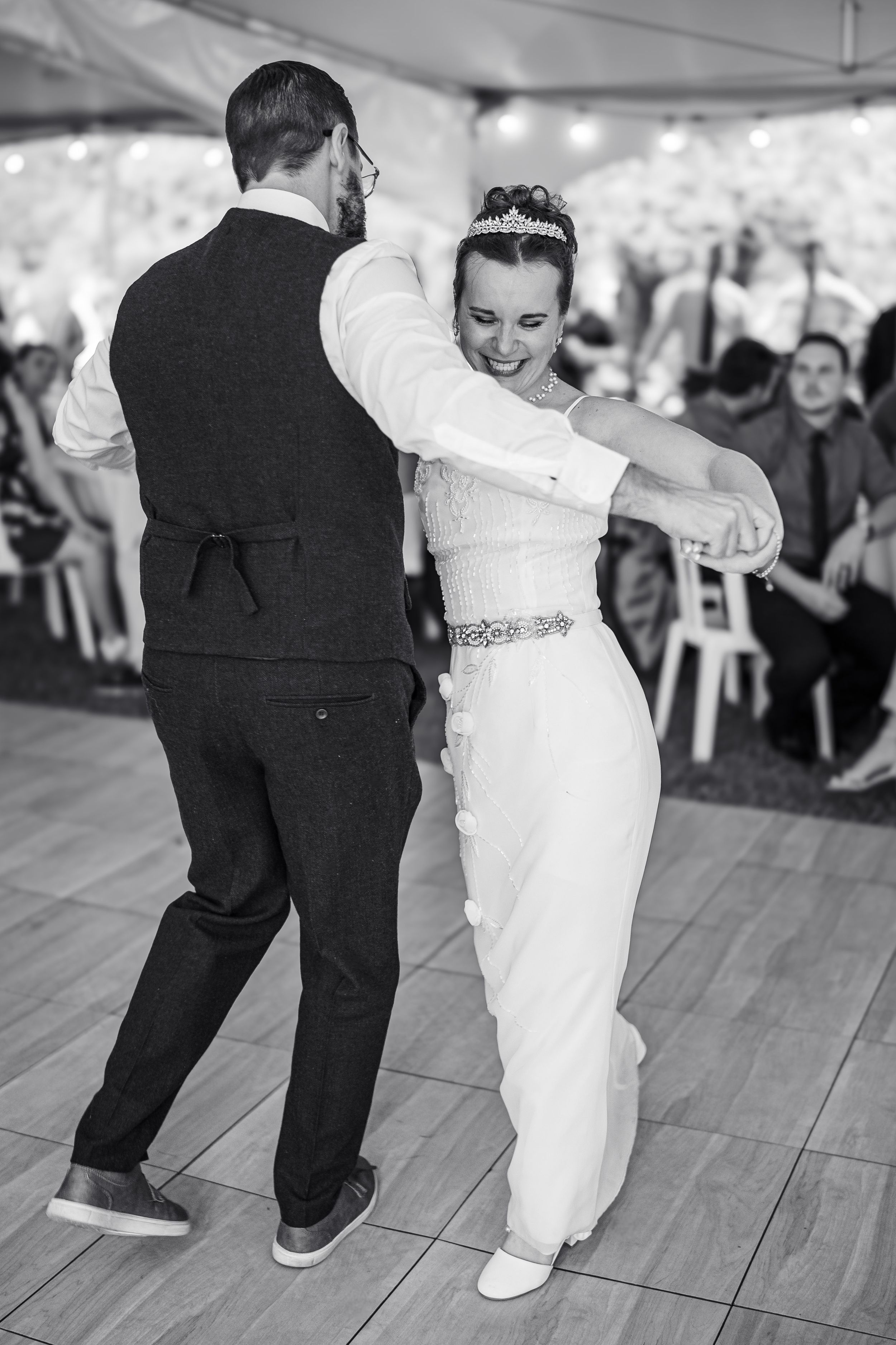 Black and white photo of bride and groom sharing their first dance at wedding reception under a tent.