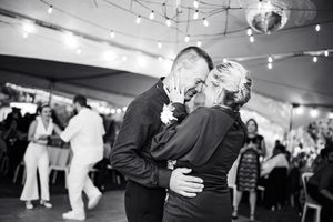 Black and white photo of a couple sharing a romantic dance embrace at a wedding reception under string lights.