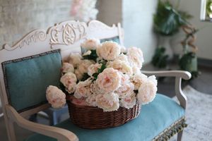 A wicker basket filled with soft pink roses resting on a vintage teal cushioned chair in an elegant room.