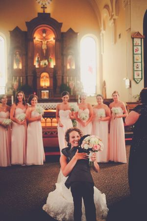 Bride and child holding bouquet in church with bridesmaids in pink gowns standing at altar during wedding ceremony.