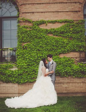 Bride and groom share a romantic moment in front of an ivy-covered brick wall on their wedding day.