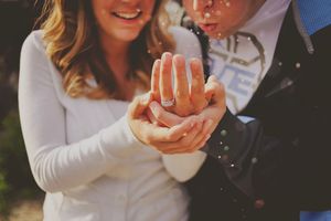 Couple showing off engagement ring with diamond band, hands together in romantic proposal moment.