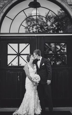 Black and white photo of a bride and groom sharing a kiss outside elegant wooden doors on their wedding day.