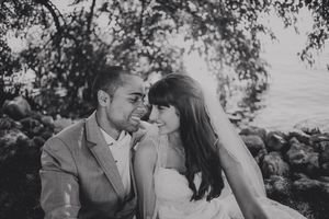 Black and white photo of a couple in wedding attire sharing a romantic moment outdoors near rocky shoreline.