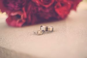 Two silver wedding rings and a diamond engagement ring on a white surface with red roses bouquet in background.