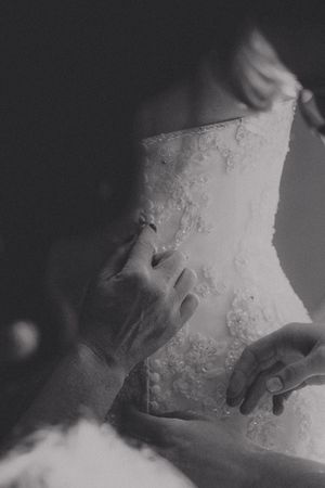 Black and white photo of hands fastening buttons on a lace wedding dress corset back.