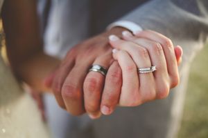 Newlywed couple holding hands showing matching silver wedding bands and diamond engagement ring closeup.