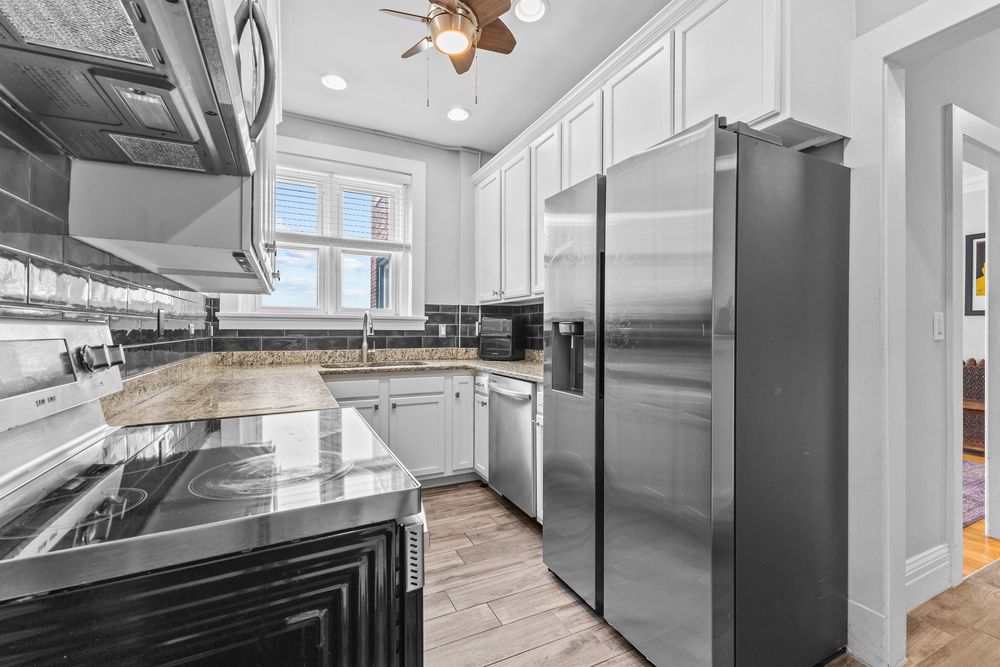 Spacious kitchen featuring white cabinetry, stainless steel refrigerator, granite counters, and ceiling fan.