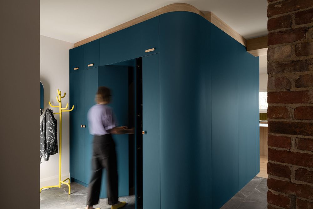 Person entering a teal blue built-in cabinet room divider beside exposed brick wall in modern interior design.