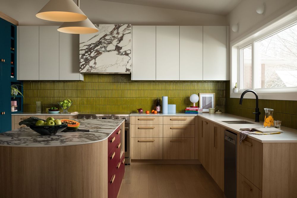Modern kitchen with olive green tile backsplash, marble hood, wood cabinets, burgundy island, and light wood floors.
