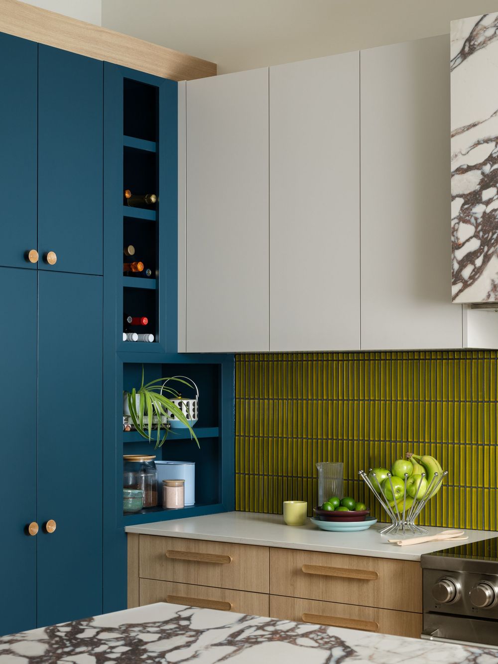 Contemporary kitchen featuring teal blue cabinets with brass hardware, olive green tile backsplash, and wood lower cabinets.