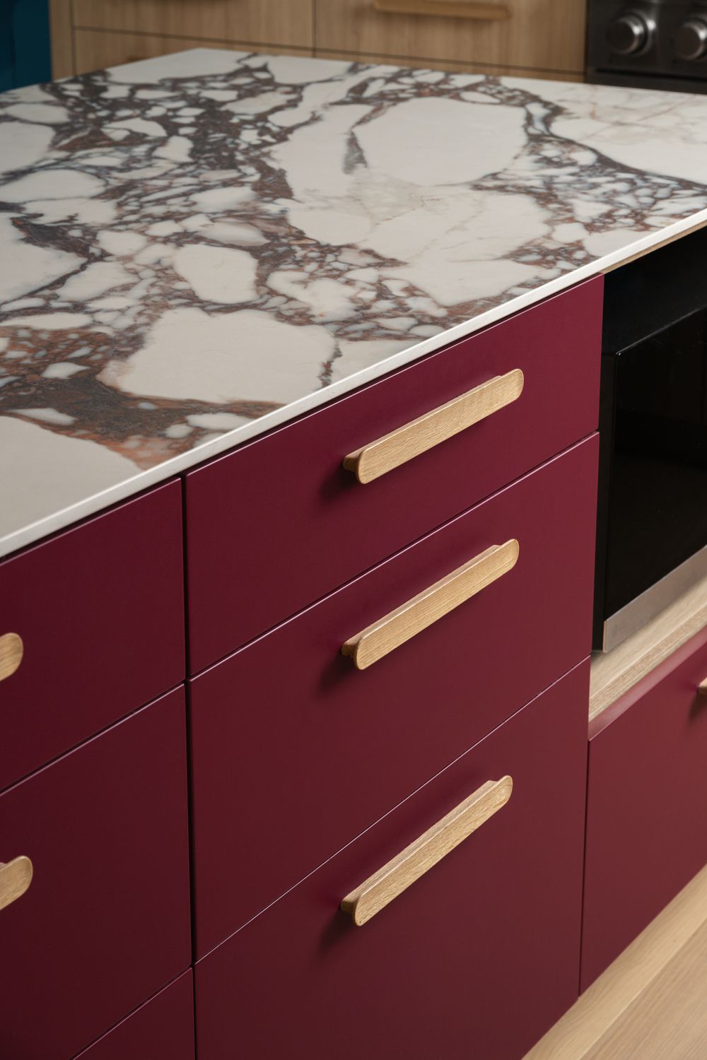 Deep burgundy kitchen drawers with wooden handles beneath a white and purple marble countertop.