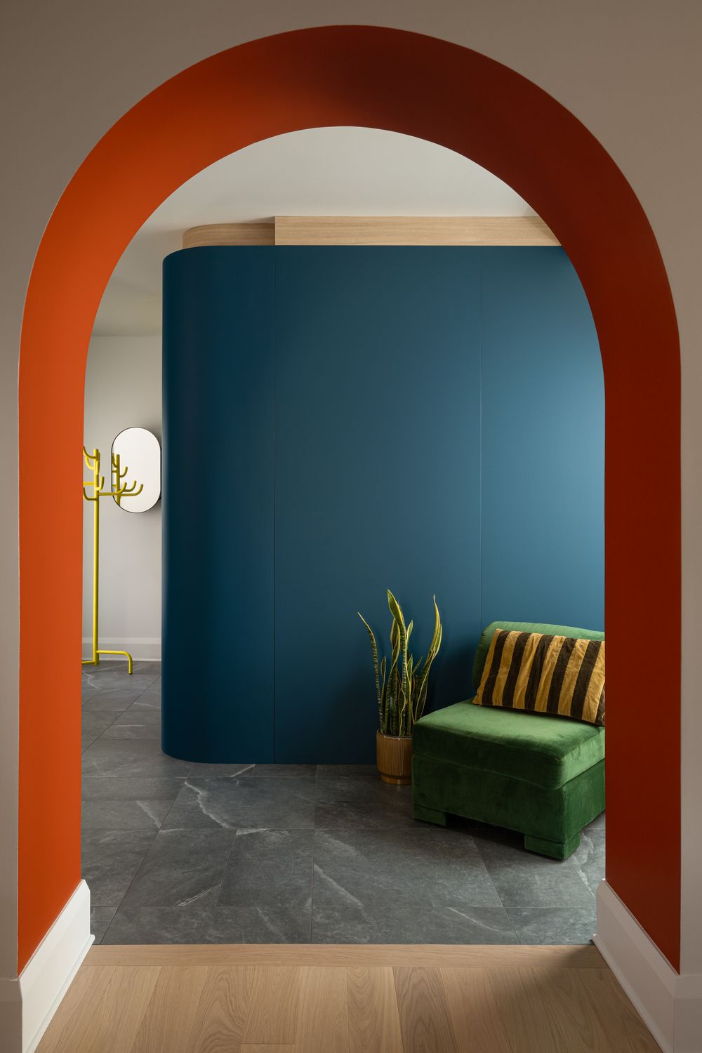 Bold interior with orange arched doorway, teal accent wall, green velvet chair, and gold floor lamp on gray marble tiles.