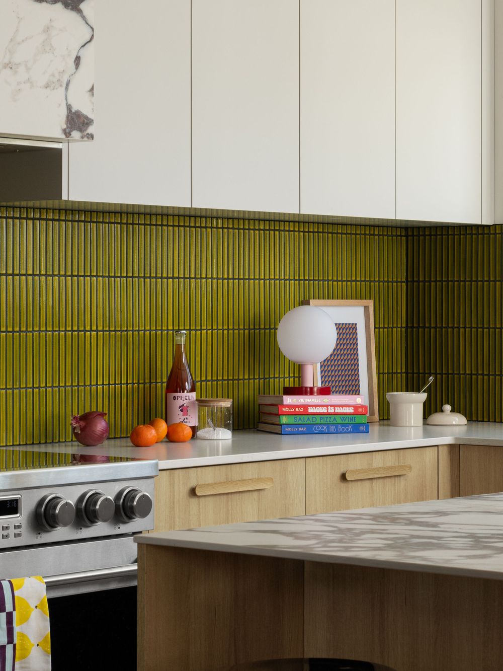 Modern kitchen with olive green stacked tile backsplash, stainless steel range, wood cabinets, and white quartz countertops.