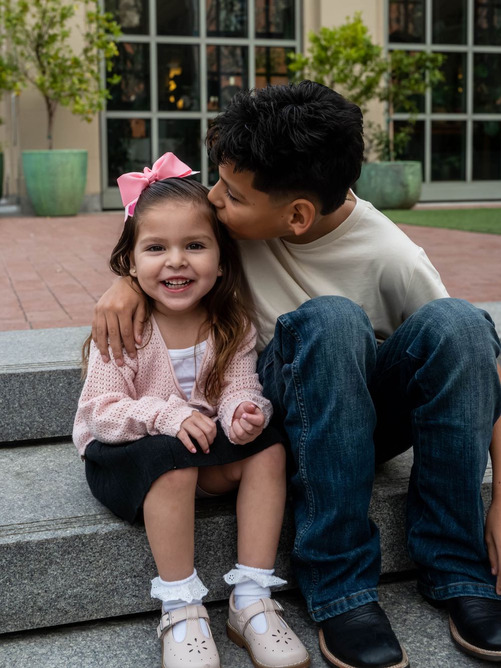 Young boy kissing his little sister on the cheek as they sit together on outdoor steps.