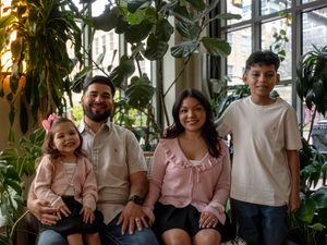 Happy family of four posing together indoors surrounded by lush green tropical plants.