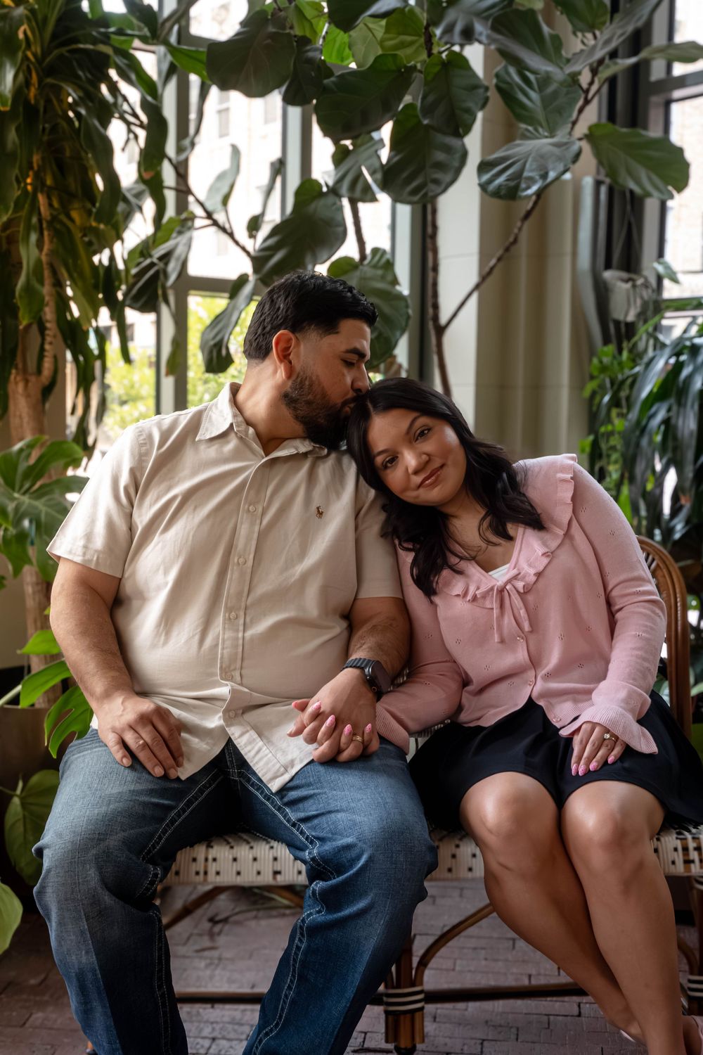 Couple sitting together on bench surrounded by lush indoor plants in cozy setting.