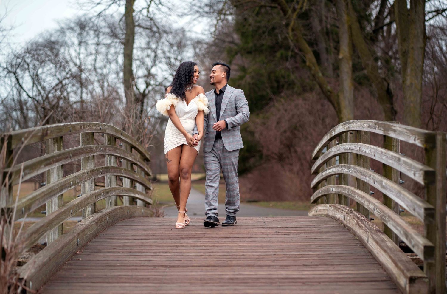 A couple shares a romantic embrace outdoors, man kissing woman's cheek as she smiles in elegant white dress.