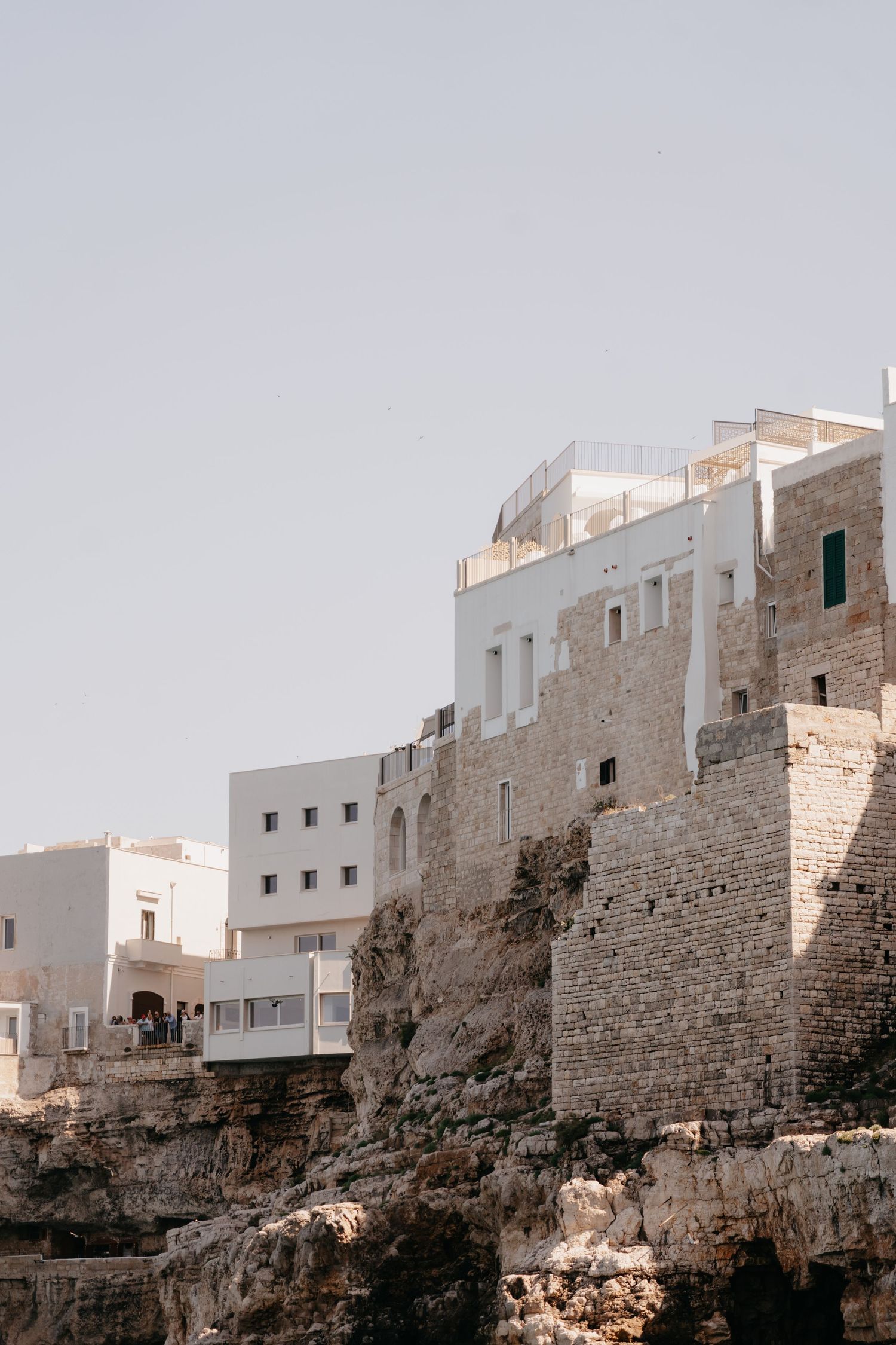 White buildings perched atop ancient limestone cliffs in Polignano a Mare, Italy, under a clear sky.