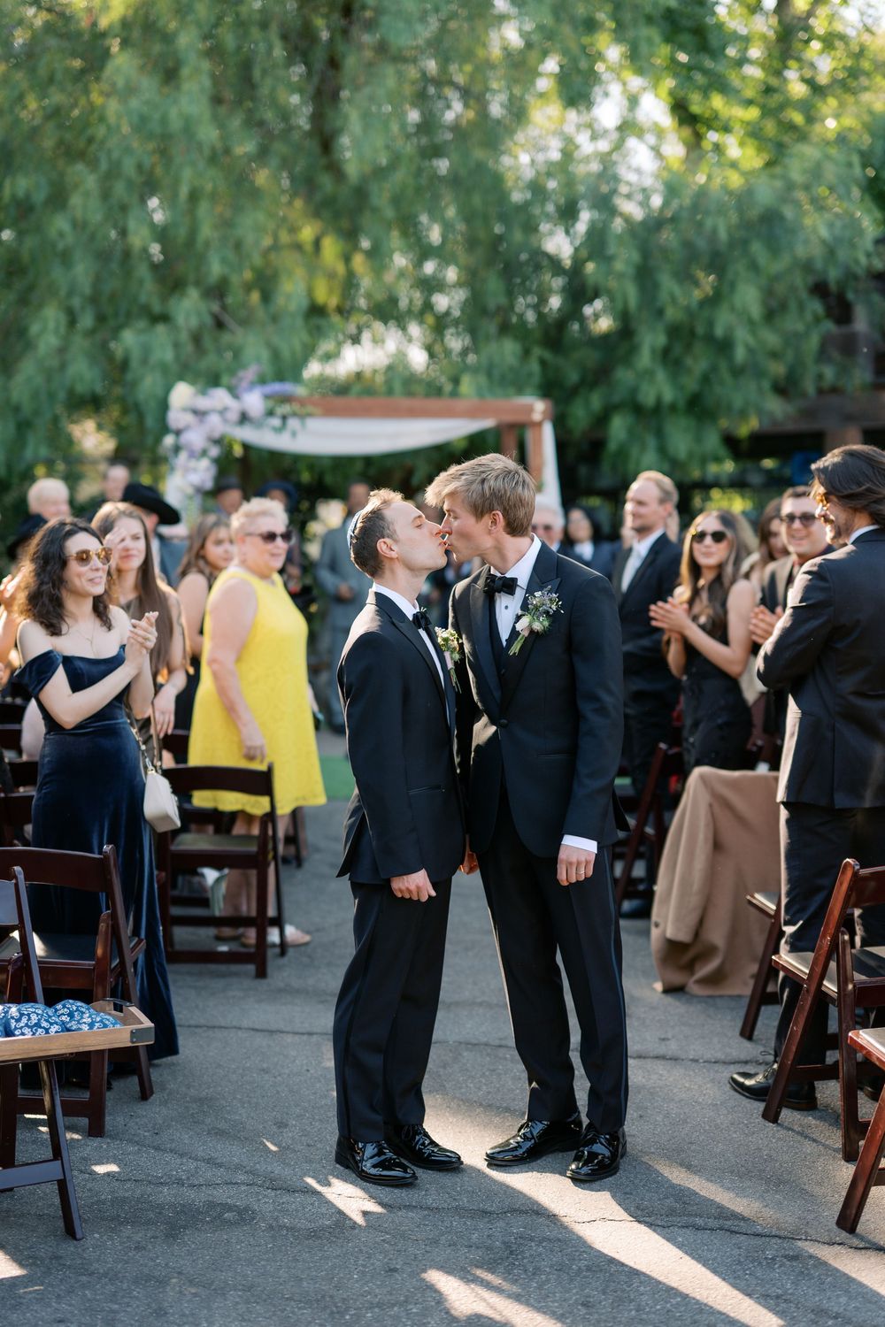 Two grooms share their first kiss as a married couple during an outdoor wedding ceremony.