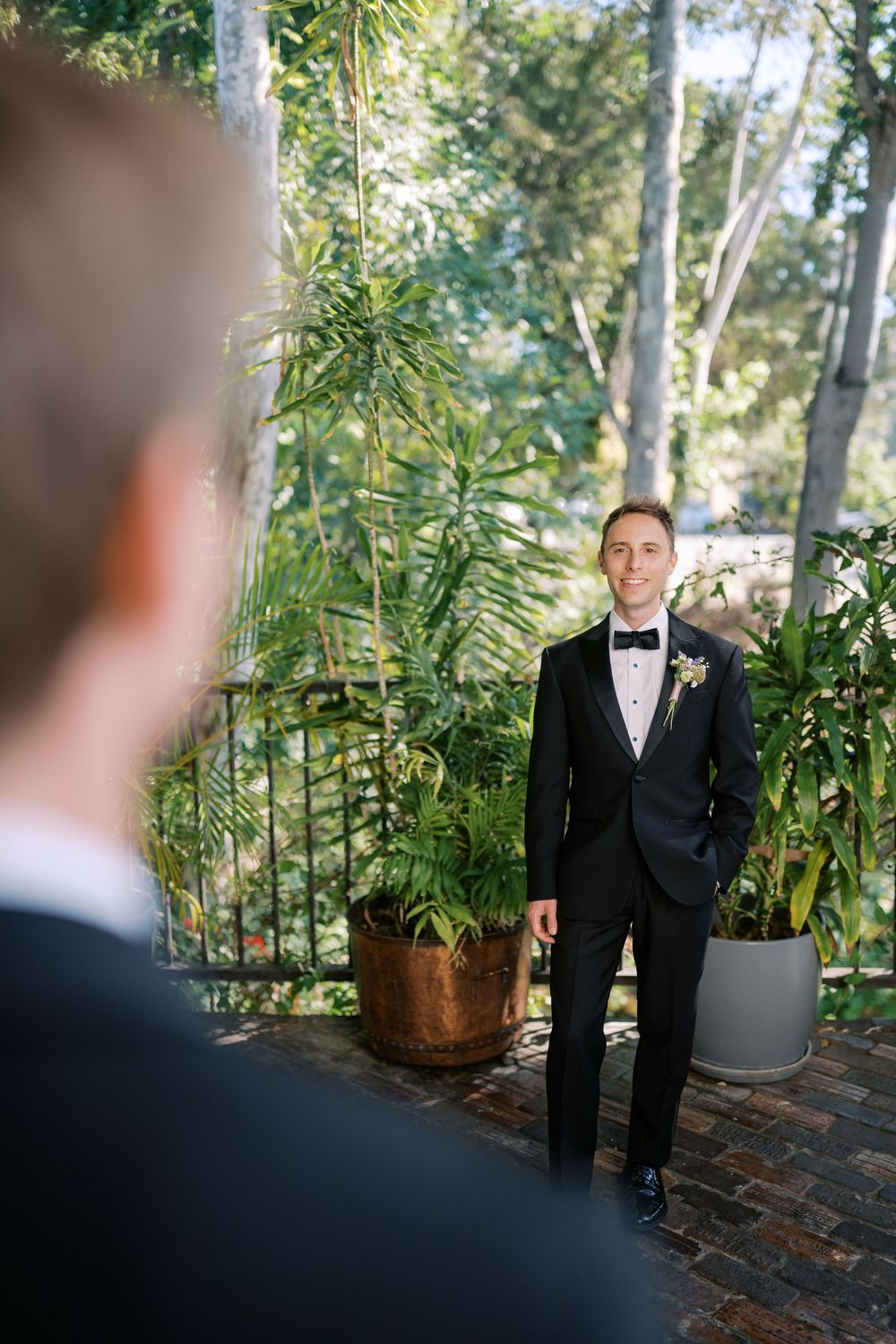 Groom in black tuxedo with boutonniere smiles during an emotional first look moment at outdoor wedding.