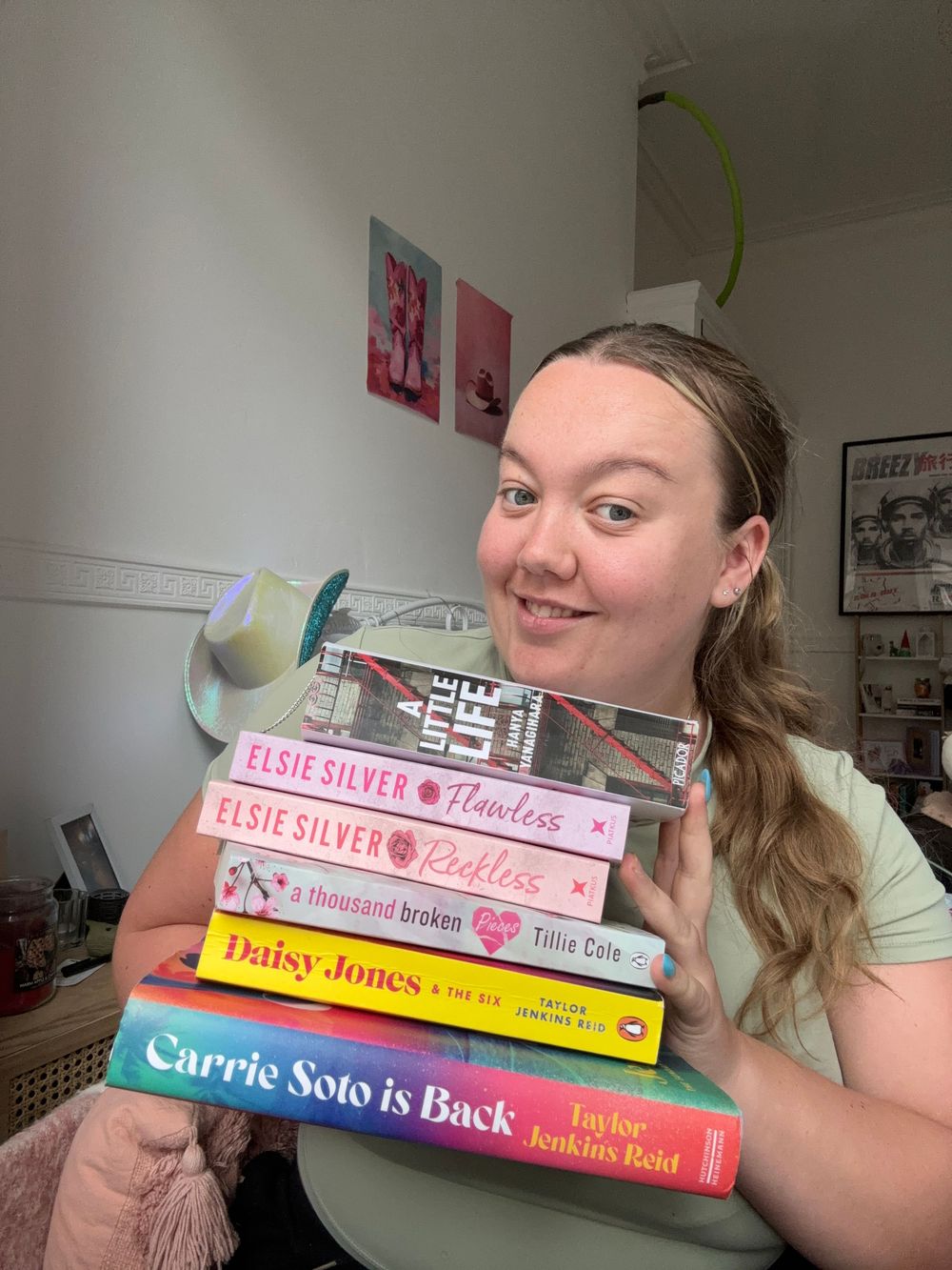 Smiling woman holding a stack of romance novels including titles by Elsie Silver and Taylor Jenkins Reid.