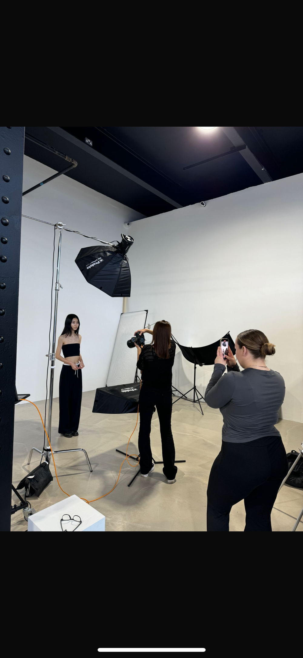 Behind the scenes of a professional photo shoot in a white studio with lighting equipment and photographers.