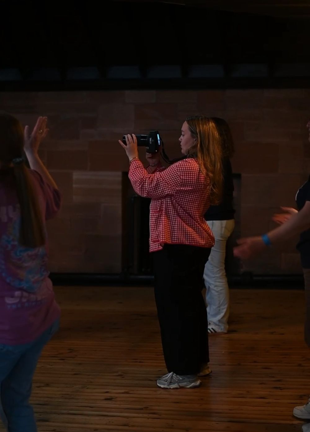 Photographer capturing images in a dimly lit venue while people dance around her.