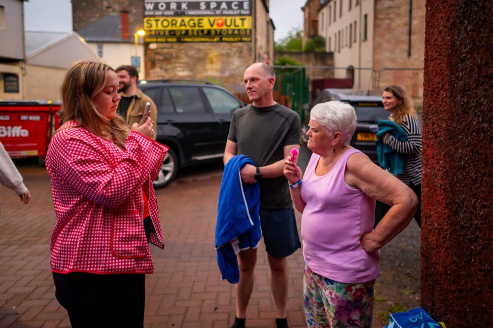 A group of people chat outdoors near a Storage Vault building on a cloudy day.