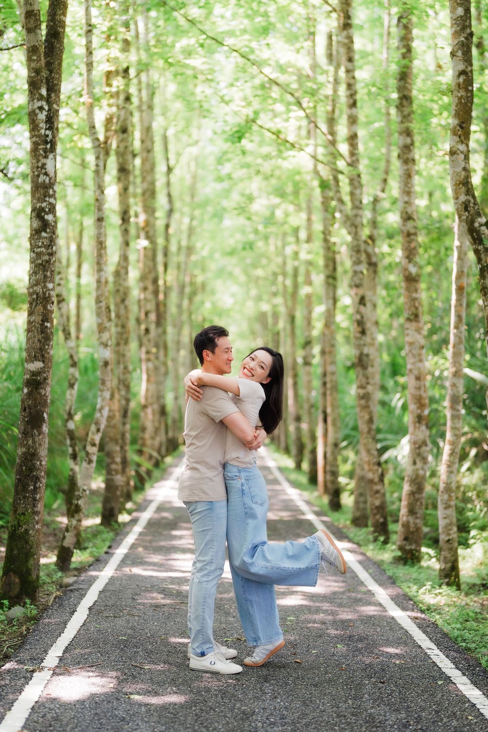 Romantic Asian couple embracing and hugging on a beautiful tree-lined pathway in a green forest.