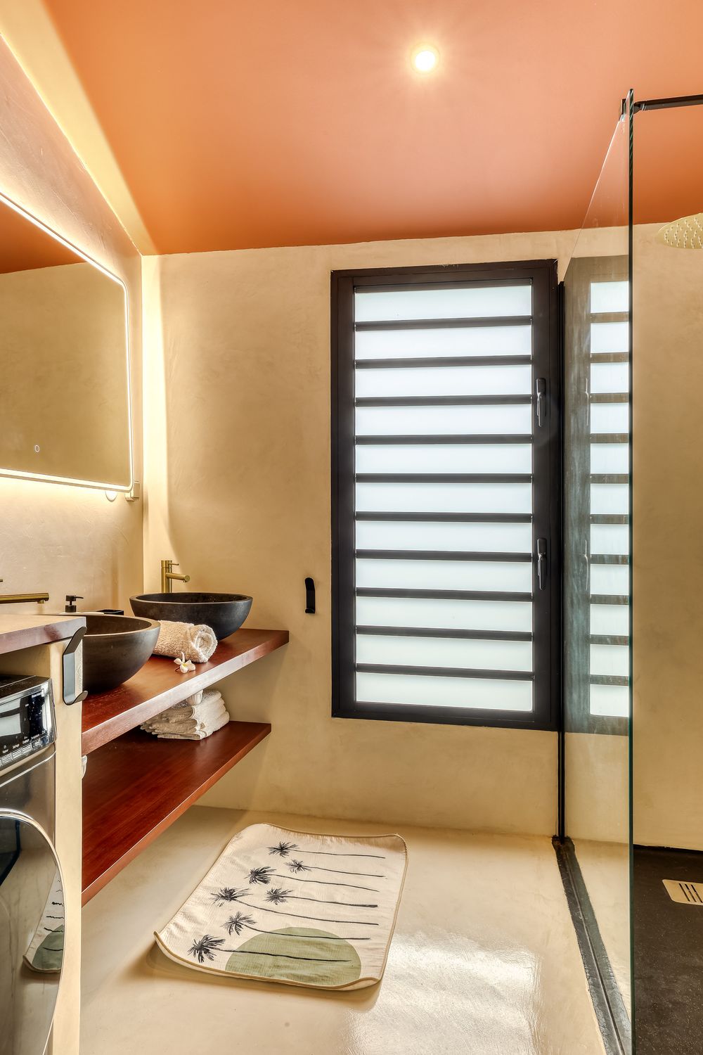 Modern bathroom with orange ceiling, vessel sink, wood vanity, walk-in shower, and louvered window.