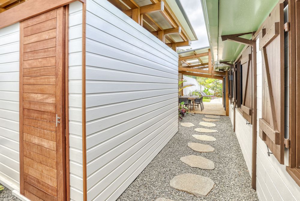 Covered outdoor walkway with stepping stones, wood-paneled walls, and lush garden views at a tropical property.