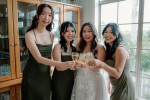 Bride in white gown toasting champagne with three bridesmaids in olive green dresses at a wedding celebration.