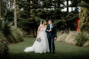 Bride and groom sharing romantic moment in lush garden with tall pine trees backdrop.