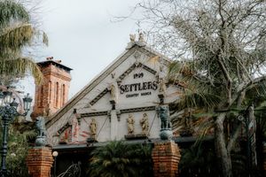 Historic Settlers Country Manor building facade with ornate decorations, brick walls, and lush trees under overcast skies.