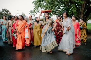 Women in colorful traditional Indian attire dance joyfully outdoors during a festive wedding celebration ceremony.