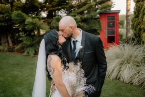 Bride and groom sharing a romantic kiss outdoors, with a red phone booth and lush greenery in the background.