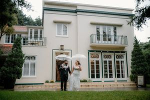 Bride and groom standing outside elegant white two-story wedding venue with balconies and French doors.