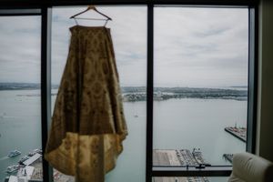 Gold brocade wedding skirt hanging by a window with stunning waterfront harbor views on a cloudy day.
