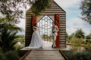 Bride and groom stand beneath a decorative arch with Maori carvings at an outdoor wedding venue in New Zealand.