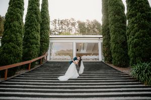 Bride and groom share a romantic dip kiss on grand striped steps flanked by tall cypress trees at elegant wedding venue.