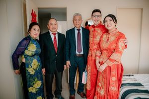 Family photo at a traditional Chinese wedding with bride and groom in red qipao and suit with elderly relatives.