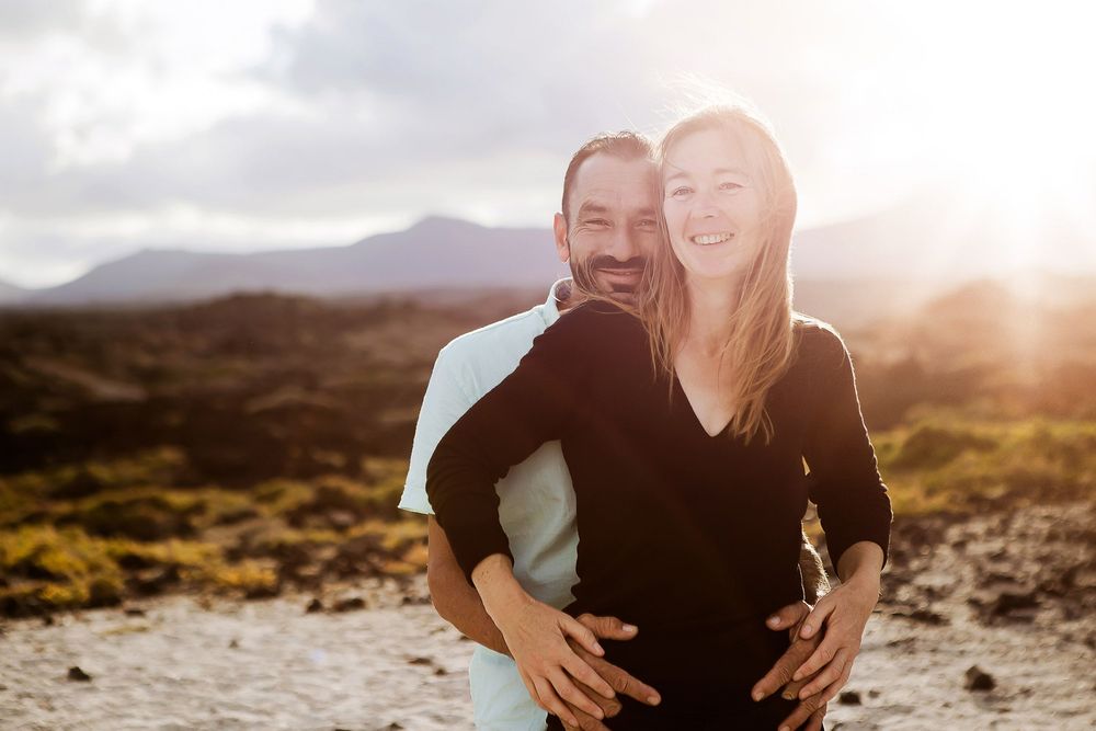 Happy couple embracing outdoors at sunset with volcanic landscape and dramatic sky in background.