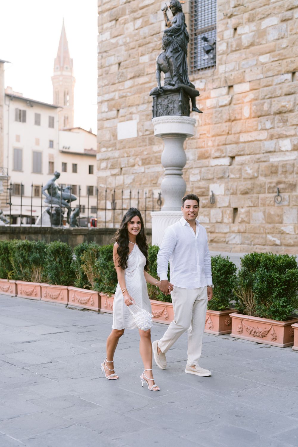 Couple in white outfits holding hands at Piazza della Signoria, Florence, Italy.
