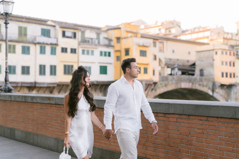 Couple in white outfits holding hands near Ponte Vecchio bridge in Florence, Italy.