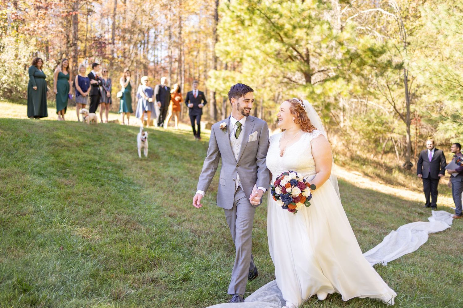 Bride and groom walk hand-in-hand on a grassy hill with guests watching in Hocking Hills Ohio.