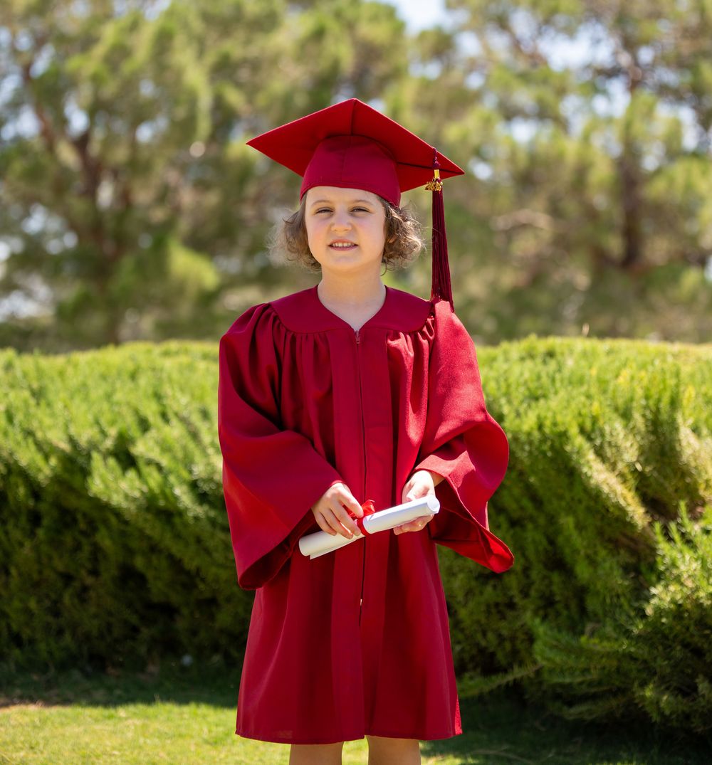 Girl in red graduation cap and gown holding diploma outdoors.