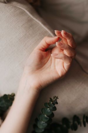 A delicate woman's hand resting gracefully on a linen cushion beside a small eucalyptus branch in soft natural light.