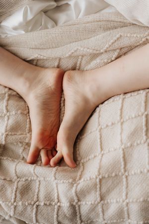 Close-up of two bare feet resting together on a soft beige quilted blanket in bed.