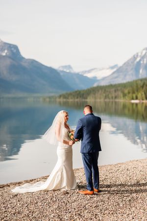 Bride and groom exchange vows on a rocky lakeshore with stunning mountain reflections in Glacier National Park.